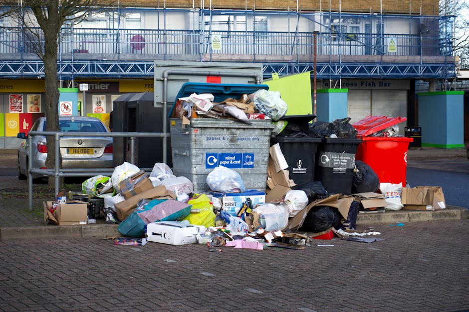 A large pile of black plastic rubbish bags is stacked against a beige tiled wall with a red spray-painted graffiti message reading 'XEND' in the background. The bags appear full and compact, with some